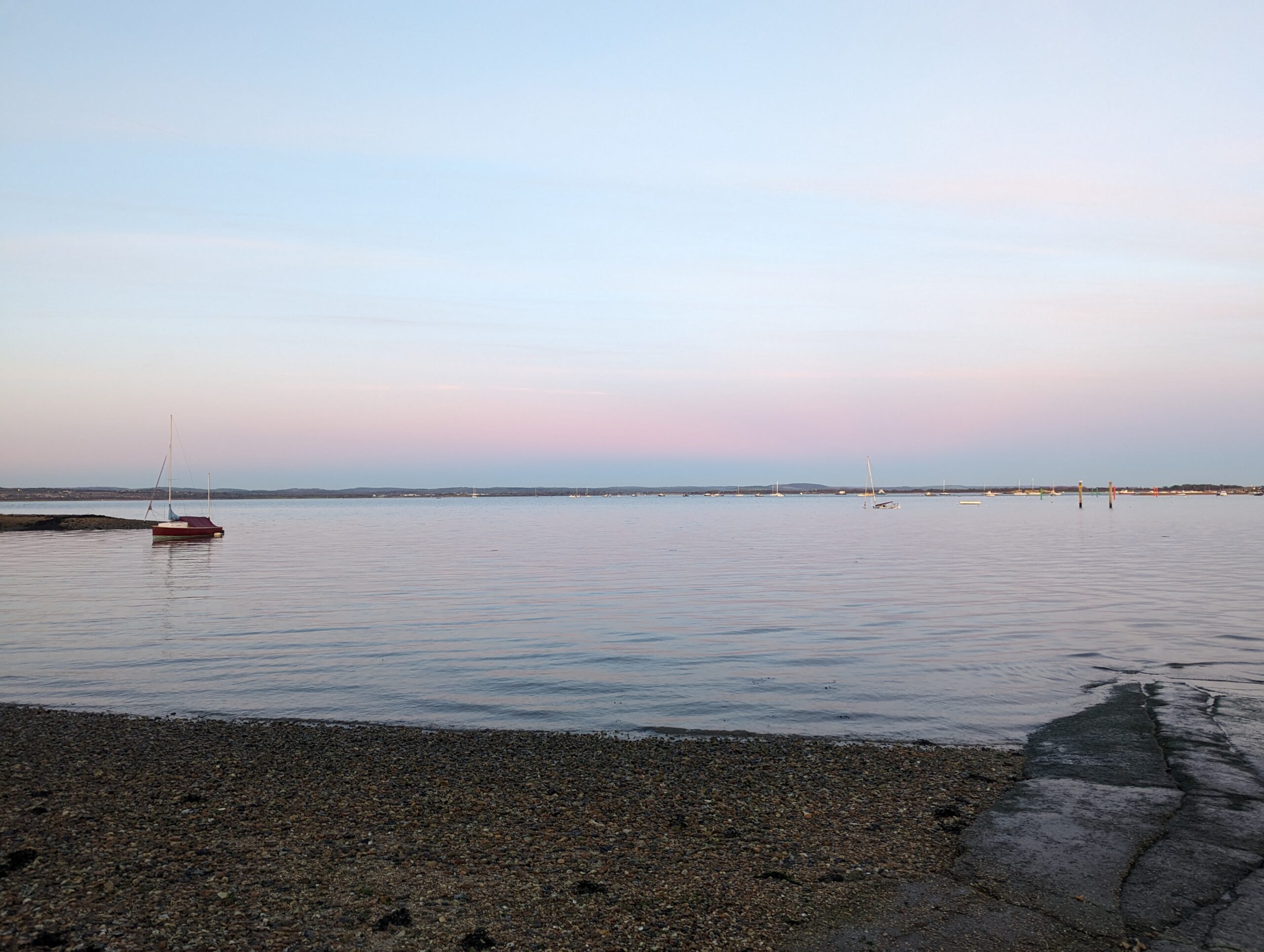 Calm blue sea with a pink blue sky and pebble beach